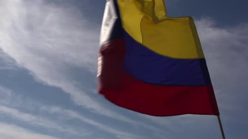 A large Colombian flag in the wind. Clouds and sun in the background.
Slow motion