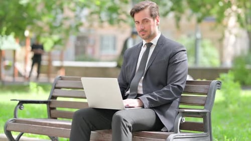 Man in Suit Works on Laptop in Park