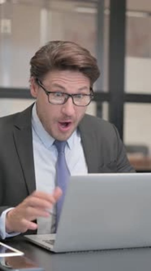 Excited Businessman Celebrating Success on Laptop in Office, vertical