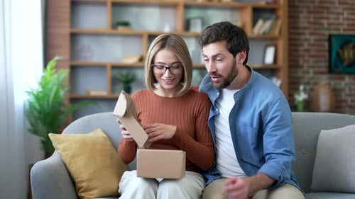 Excited Couple Opening a Gift Box on Sofa