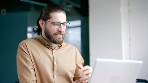 Bearded Man Video Conferencing on Laptop in Office