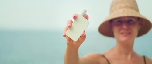 Frau im Badeanzug am Strand mit weißer Tube Sonnenschutzcreme auf Meereshintergrund.
Mädchen