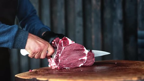 Butcher Cuts Raw Meat with a Knife