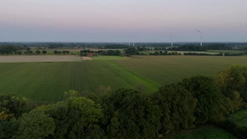 Rotating wind turbines on farm fields at dusk. American countryside with growing fields in rural