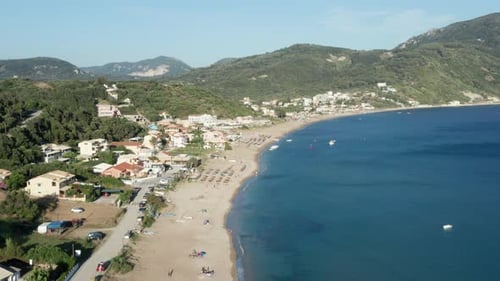 Aerial shot of a Mediterranean beach, right below the green forest covered mountains. Some buildings
