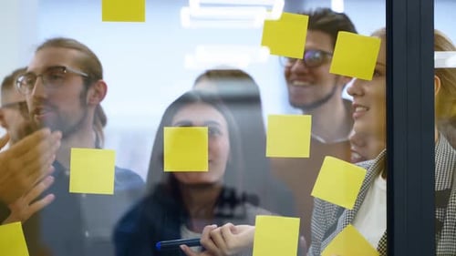 Business Team Brainstorm Writing Ideas on Paper Sticker Notes and Post It on Glass Wall Startup