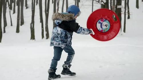 Slow motion of happy smiling boy carrying plastic sleds up the hill before sliding down on a snow