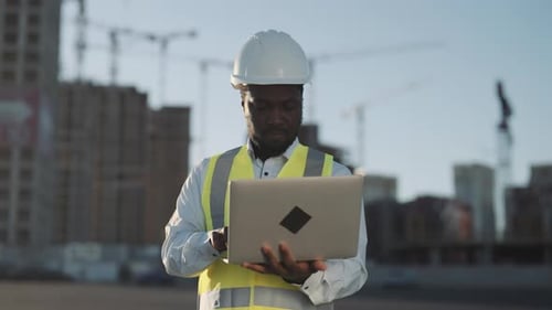 Große Baustelle mit modernen Neubauten: Vorarbeiter mit Laptop, Architekt, der das Projekt steuert