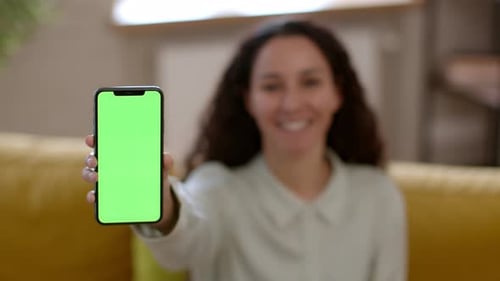 Woman Holds Smartphone with Green Screen Indoors