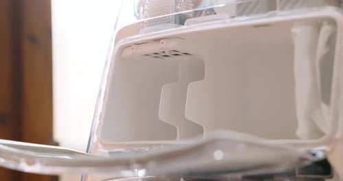 Gros plan de la main ouvrant le compartiment d'un aspirateur robot et appuyant sur le loquet du sac à poussière