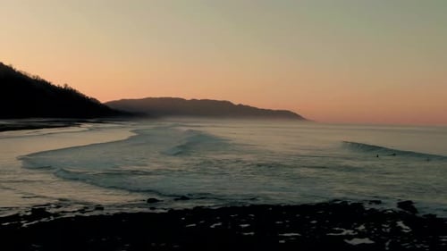Drone parallax shot of paddling surfers on tropical Costa Rica beach in sunset