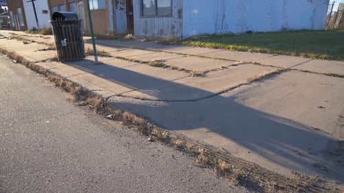 Orbiting shot of dirty city curb in Detroit with overgrown weeds and debris with long shadows during