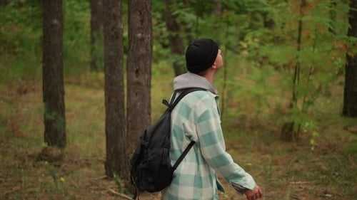 Young man walking with backpack in green forest