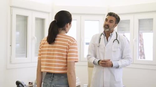 mature male doctor talking to young female patient while standing during consultation in clinic