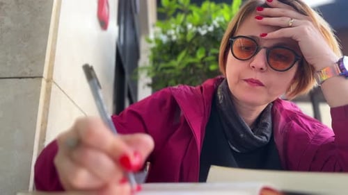 Woman Writing in Notebook at an Outdoor Cafe