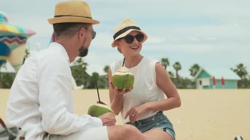 Young Cheerful Couple with Cocktails Laughing During Talk on Sandy Beach