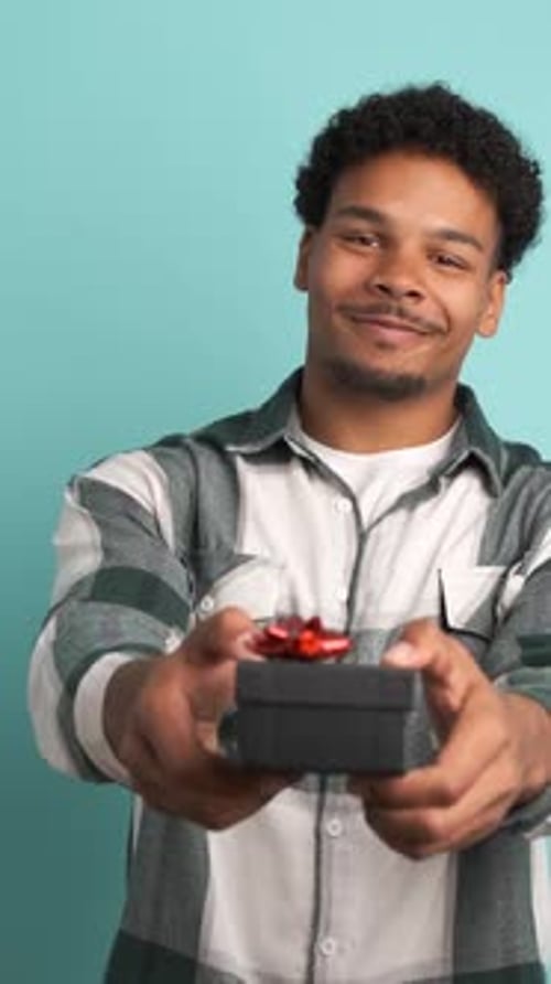 Happy Man Giving Gift Box and Looking at Camera in Blue Studio