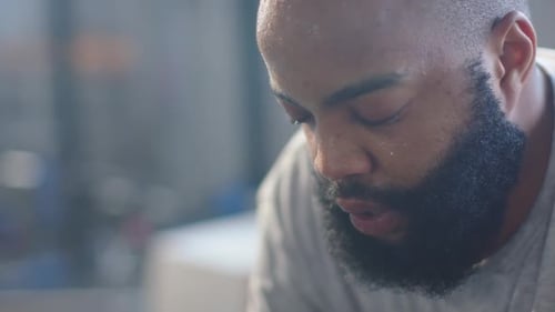 Adult man starting lowered head, breathing and steadying himself in interior with beard and sweat