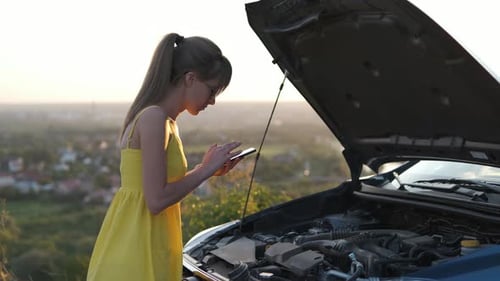 Stranded Female Driver Talking on Cell Phone Standing Near Her Vehicle with Open Hood Having Engine