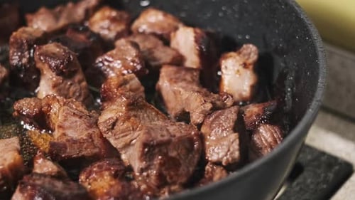 Pieces of Pork Meat are Fried in a Frying Pan in a Home Kitchen CloseUp