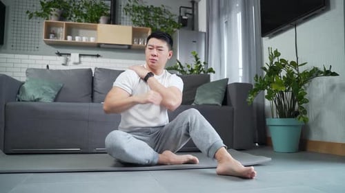Man Massaging Sore Shoulder on Yoga Mat at Home