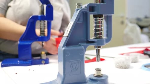 Sewer Attaching Metal Round Snaps to Clothes with Help of Manual Machine at Garment Factory