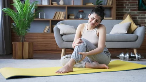 Woman on Yoga Mat Massaging Injured Knee