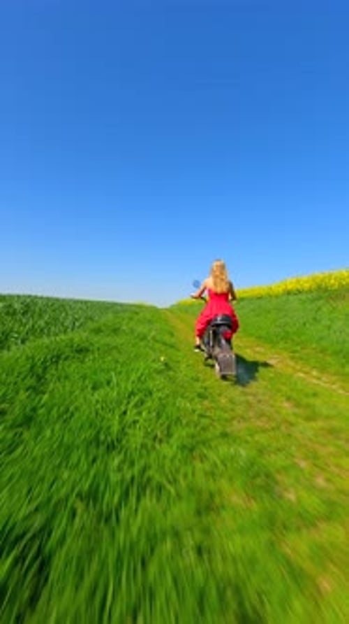 FPV of Caucasian Woman Riding a Vintage Motorcycle Through Summer Meadows