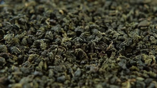 Schwarzer Trockentee-Tapetenmix aus schwarzen und grünen Teeblättern, rotierend auf einem Drehteller, Nahaufnahme, Makro, Ansicht von oben