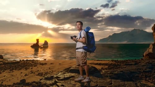 Full Body Side View Of Asian Male Hiker Holding A Camera In His Hands Then Looking Around on Beach