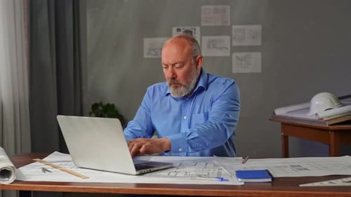 An Architect Sits in an Office at a Desk with Blueprints