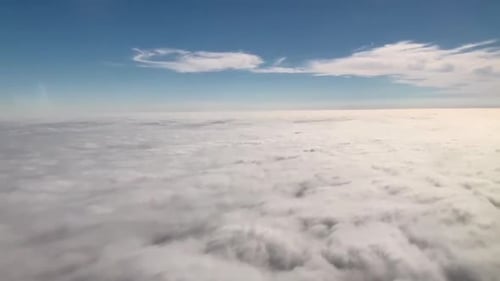 Flying over white puffy clouds on a clear blue sky day.