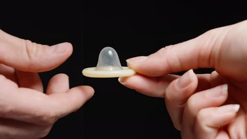 Hands Holding Condom Against Black Backdrop