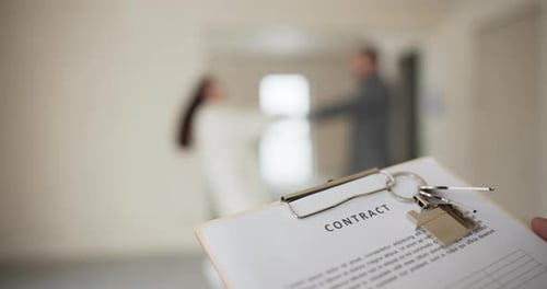 Closeup on a House Sale Purchase Agreement with Keys In the Background a Happily Married Couple