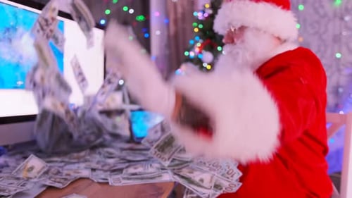 Side view of Santa with white beard in red suit throwing paper money at table with monitor