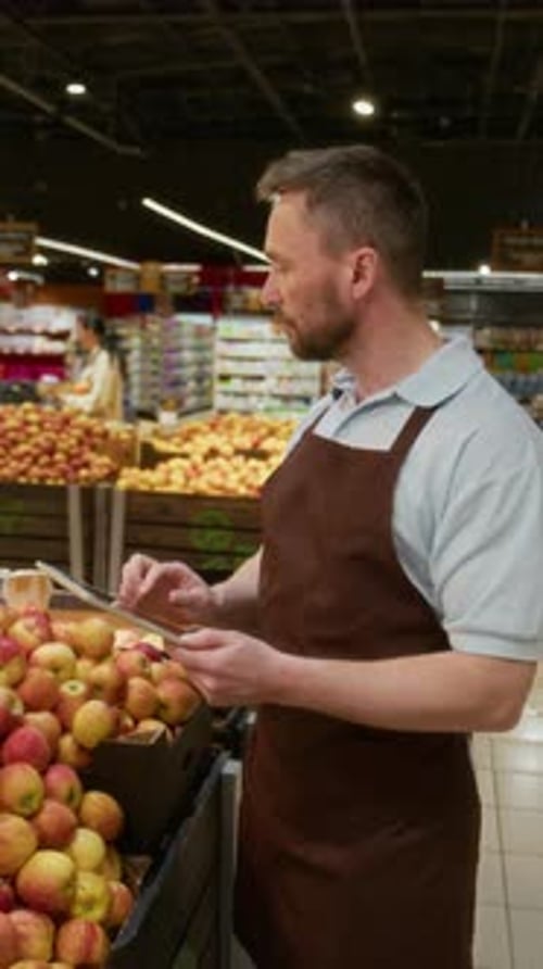 Supermarket Worker Examining Apples for Freshness and Keeping Notes on Tablet
