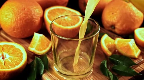 Orange Juice Pouring into Glass with Fresh Oranges