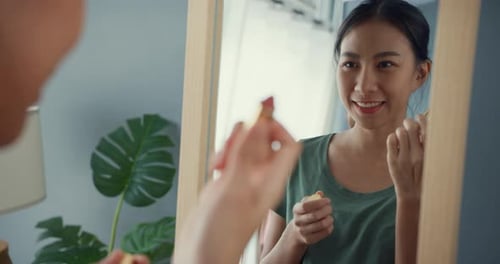 lady with casual cloth put lipstick on her lips in front of mirror in bedroom at home in morning.