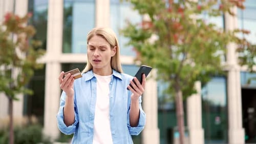 Frustrated woman discovered fraud while checking credit card on phone standing on the street near