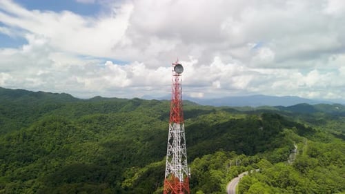 Close view shot of a tall transmission tower rising above dense forest, showcasing telecom infrast