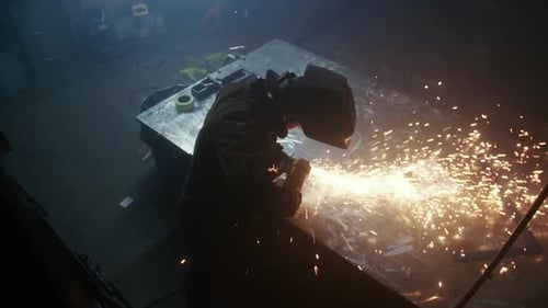 Ein Schweißer erzeugt mit einem Werkzeug auf einem Metallstück einen Funkenschauer