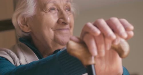 Authentic close up shot of smiling disabled senior woman with a stick is looking outside a window.