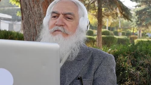 Older Man with Beard Using Laptop Outdoors