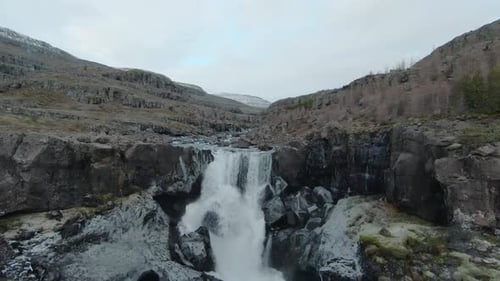 Drone flying over a beautiful, wide waterfall, towards a river full of rocks in Iceland.