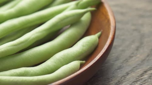 Closeup view of fresh green beans on wooden plate