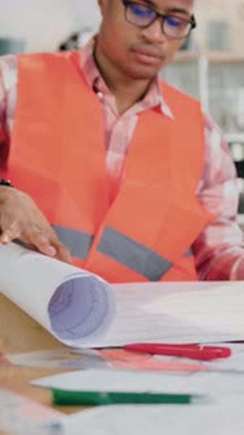 Civil Engineer Unrolling Blueprints on Desk Indoors