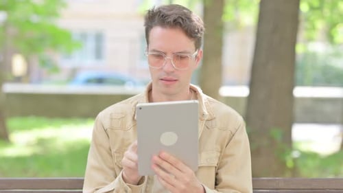 Young Man Uses Tablet in Urban Green Park