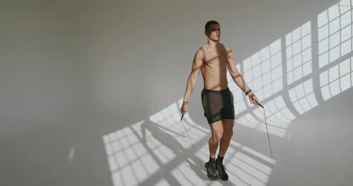 Athletic Man Exercising with Jumping Rope at Studio with White Background