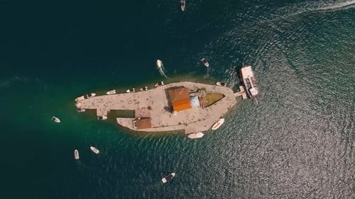 Aerial drone view approaching Our Lady of the Rocks island with a church, tourists, and boats in the