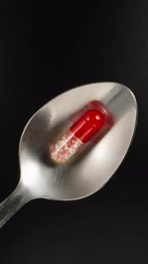 Red and white pill, capsule on a spoon, black background, top view. Dolly slider extreme close-up. L